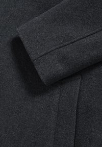 Mörkgrå ulljacka med en mjuk, texturerad yta. Synlig ärm med en ren sömdetalj som visar en vikt manschettdesign.