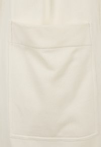 Cream-colored fabric featuring a textured surface with a prominently stitched pocket on the front. The stitching is contrasting and neat.