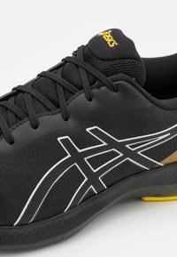 Černá sportovní bota s texturovaným svrškem, z materiálů síťoviny a syntetiky, kontrastními bílými a žlutými akcenty a odolnou gumovou podrážkou.