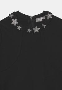 Top nero con scollatura rotonda decorata con un colletto di stelle argento e nere. Chiusura a zip sul retro, tessuto dalla texture liscia.