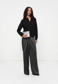Zwarte lange mouwen top met een V-hals; grijze metallic wijde broek; zilveren clutch met ketting; gladde texturen en minimalistisch ontwerp.