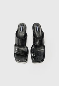 Sandales noires avec un motif crocodile, présentant une large bride et un bout carré. Texture lisse avec un léger éclat. Logo visible sur la semelle intérieure.
