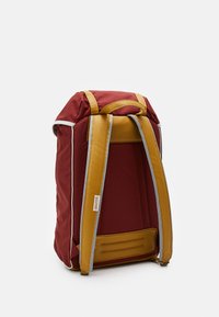 Sac à dos en tissu rouge avec des accents en cuir jaune. Il dispose d'un dos rembourré, de bretelles ajustables et d'un design moderne et épuré avec des coutures contrastées.