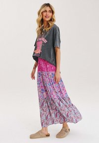 Šedé zkrácené tričko s růžovou grafikou, oblečené přes dlouhou sukni s růžovým a modrým paisley vzorem. Béžové slip-on boty s nízkým podpatkem.