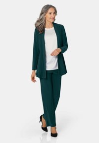 Donkerblauwe outfit bestaande uit een lange cardigan en wijde broekspijpen, gecombineerd met een witte top met kleine versieringen. Zwarte hakken.