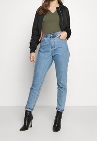 Czarna bomberka z pomarańczowym wykończeniem, oliwkowy top z dekoltem w serek, wysokogatunkowe jasnoniebieskie dżinsy i czarne błyszczące botki za kostkę.