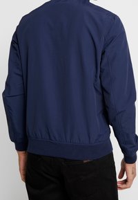 Námorně modrá lehká bomber bunda s pleteným pasem a manžetami, hladkým povrchem a jednoduchým designem bez ozdob.