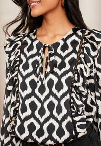 Blusa a righe bianche e nere con maniche a volant, scollatura a chiave e tessuto testurizzato con una leggera lucentezza.