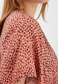 Krátký rukáv top v rzi s texturovaným vzorem černých a bílých teček, s volnějším střihem a měkkou tkaninou.