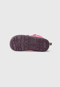 Scarpa rosa per bambino con suola texturizzata viola scuro e logo del marchio, esposta con la parte inferiore rivolta verso l'alto su uno sfondo chiaro e semplice.