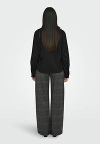 Maglietta nera a maniche lunghe con spalle scese abbinata a pantaloni a gamba larga grigi a quadri, dotati di vita elastica e tasche laterali.