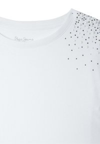 Camiseta de algodón blanca con escote redondo y adornos dispersos de pequeñas tachuelas plateadas y perlas en un hombro.