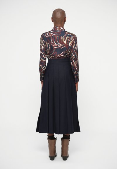 Långärmad skjorta med ett färgglatt, abstrakt mönster i kombination med en marinblå, veckad kjol. Bruna ankelstövlar med en texturerad ovandel.