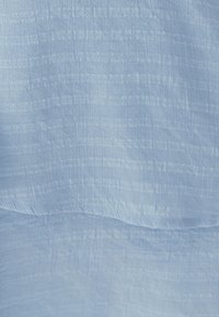 Šviesiai mėlyna medžiaga su tekstūruota, raukšlėta paviršiumi. Medžiaga atrodo minkšta su subtiliu blizgesiu, demonstruojančiu menkas horizontalias linijas.