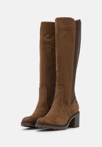 Botas marrones hasta la rodilla con acabado de ante, que cuentan con una cremallera lateral y un panel elástico marrón en contraste, punta redonda y tacón grueso.