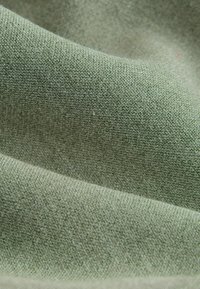 Gros plan sur un tissu vert doux avec une surface tissée texturée et des plis doux créant des ombres et des reflets.