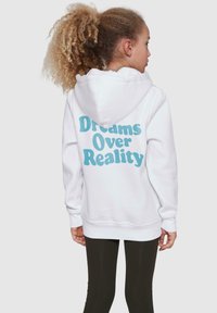 White hoodie featuring blue text "Dreams Over Reality" on the back, with a soft texture and a drawstring hood. Worn with dark leggings.