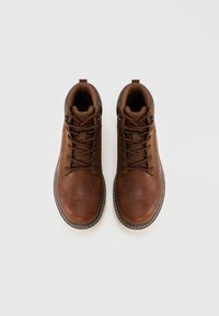 Botas de tobillo de cuero marrón con punta redonda, superficie texturizada, diseño con cordones y costuras blancas contrastantes a lo largo de la suela.