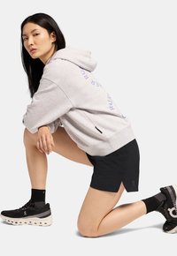 Grau Hoodie mit lockerer Passform, mit blauer Schrift; schwarze Shorts; schwarz-weiße Sport Schuhe mit gemusterten Akzenten.
