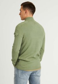 Grüner Strickpullover mit hohem Kragen, gerippten Bündchen und Patches detail an den Ärmeln. Glatte Textur, slim fit und minimales Branding.