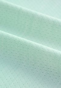 Ljus mintgrönt tyg med ett texturerat mönster, bestående av små, jämnt fördelade prickar. Materialet ser mjukt och något elastiskt ut.