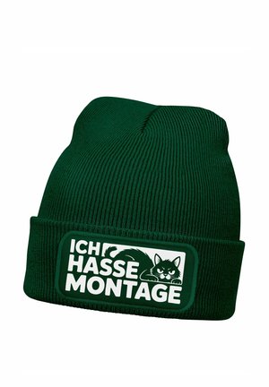 Grüne Strickmütze mit geripptem Muster, versehen mit einem rechteckigen Aufnäher, auf dem der Text "ICH HASSE MONTAGE" und eine Katzenabbildung zu sehen sind.