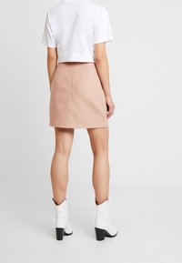 Rosa skaterkjol med en mjuk textur, bakre dragkedjedetalj, i kombination med en vit kortärmad t-shirt och vita klackstövletter.