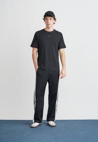 Μαύρο αθλητικό t-shirt με κοντά μανίκια, συνδυασμένο με μαύρο παντελόνι φόρμας με λευκές ρίγες. Το λευκό casual παπούτσι ολοκληρώνει την εμφάνιση.