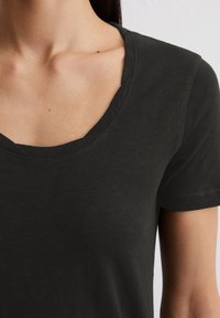 T-shirt en coton noir avec un décolleté en V profond, des manches courtes et une texture douce et lisse. Présente des détails de couture minimalistes.