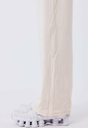 Witte sportschoenen hebben een mesh bovenkant met getextureerde accenten en een onderscheidende gewatteerde zool. Lichtbeige, gestroomlijnde broek past perfect bij de uitstraling.