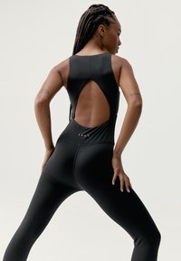 Svart aktivklädedräkt med rund halsringning och stor utskärning på baksidan, tillverkad av slät tyg, med minimala sömnadsdetaljer.