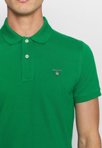 Polo verde realizzato in cotone testurizzato, con colletto classico, due bottoni e un piccolo logo ricamato sul petto.