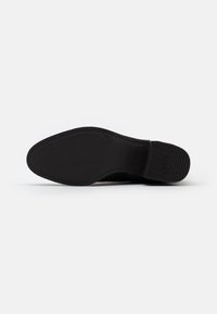 Suela de zapato negra, material de goma suave, patrón de agarre texturizado, tacón plano, logo embosado en el lateral y marcaje de tamaño visible.