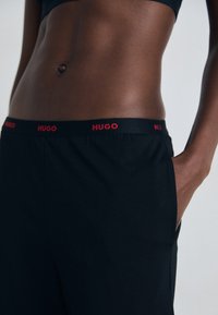 Svart byxor med röd "HUGO" midja, med en slät yta och skräddarsydd passform, med sidofickor och en minimalistisk design.