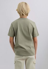 Camiseta de algodón de manga corta en color verde oliva, de corte recto y cuello redondo, combinada con pantalones de color claro.