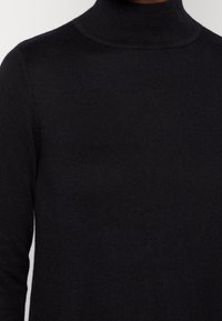 Maglione a collo alto nero realizzato in tessuto a coste, con un design aderente e maniche lunghe. Texture morbida con una finitura liscia.