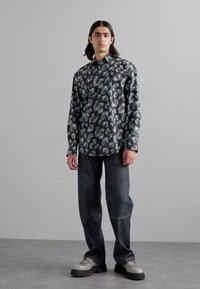 Black floral-patterned button-up shirt, long sleeves, paired with blue denim pants. Worn with chunky gray and black shoes.