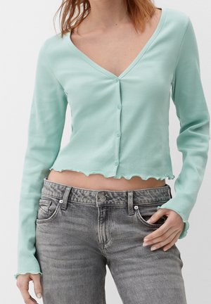 Cardigan court côtelé vert menthe avec un décolleté en V, fermeture à boutons et ourlet ondulé. Associé à un jean gris taille haute avec poches.