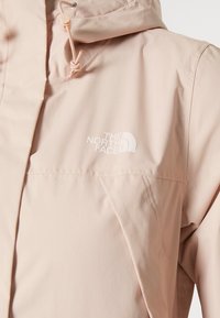 Giacca impermeabile rosa chiaro realizzata in tessuto liscio. Include logo del marchio, cappuccio regolabile con cordino e tasca frontale.