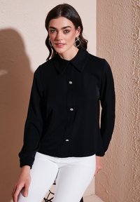 Black button-up shirt with a collar, featuring crystal-like buttons, paired with white pants. Smooth fabric and long sleeves.