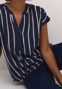 Blouse boutonnée bleu marine à rayures verticales blanches, manches courtes et col mandarin. Tissu doux avec une coupe décontractée.