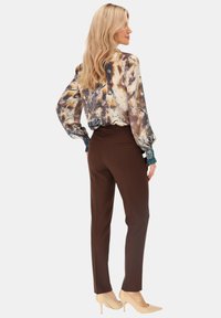 Bluzka z długim rękawem w wielokolorowy kwiatowy wzór, zestawiona z dopasowanymi brązowymi spodniami oraz cielistymi szpilkami.