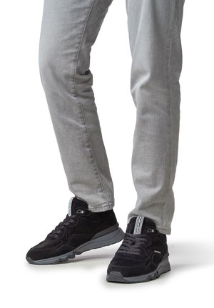 Sneakers in suede nero con suole in gomma grigia, caratterizzate da una superficie testurizzata e dettagli bianchi a contrasto vicino ai lacci e alla linguetta.