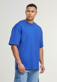 Blå bomulds-t-shirt med rund hals og korte ærmer, der har en afslappet pasform og glat tekstur. Båret med lyse vaskede cargo shorts.