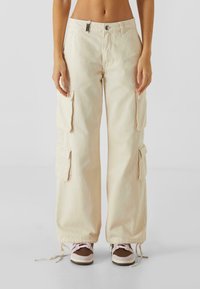 Beige cargo bukser med brede ben, lavet af denim, med to sidelommer, justerbare linninger og lynlås lukning.