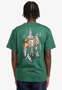 Green cotton t-shirt featuring a detailed graphic print on the back, depicting multiple figures with varying poses and facial expressions.