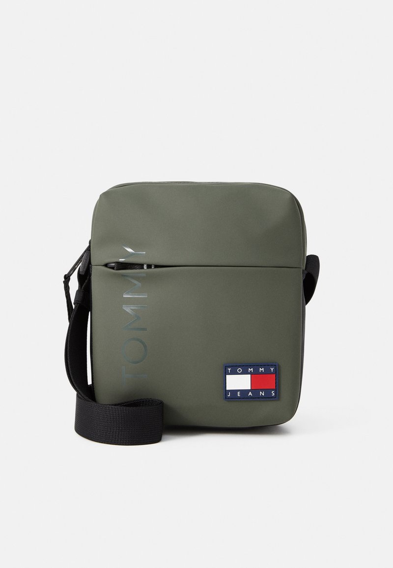 Grüne wasserdichte Crossbody-Tasche mit Reißverschluss, ausgestattet mit einem Logo-Druck und weitem Aufnäher. Schwarzer verstellbarer Gurt und strukturierte Oberfläche. Kompaktes Design.