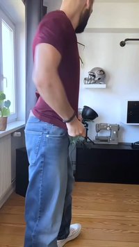 Blue jeans de denim com um corte relaxado, combinados com uma t-shirt cor de burdeos. O cenário apresenta um chão de madeira e uma máquina de costura ao fundo.