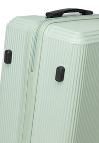 Hard-shell suitcase in light mint green, featuring a textured surface with vertical ridges, black zippers and hardware accents.