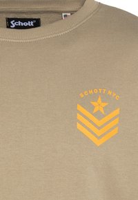 Beżowa bawełniana bluza z prążkowanym, okrągłym dekoltem, pomarańczową grafiką z tekstem i gwiazdą oraz wzorami w jodełkę na przodzie.